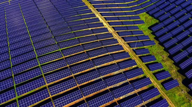 Diagonal rows of solar panels cross rural field. Aerial perspective highlights dirt paths and grassy strips between modules.