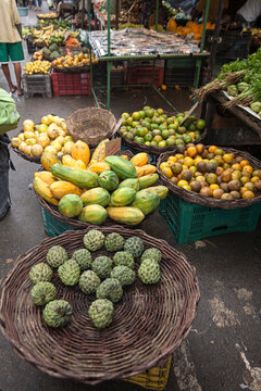 Frutas tropicais expostas em cestos de vime em feira livre brasileira, com mam&atilde;o, pinha, laranja e outras frutas frescas, retratando o com&eacute;rcio popular e a agricultura regional.