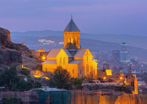 Evening view of Saint Nicholas Church below Narikala Fortress with the modern skyline of Tbilisi, Georgia.