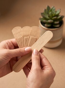 Medical adhesive bandages and wooden tongue depressor held in hands, first aid supplies for wound care and healthcare, beige fabric plasters for skin protection and healing 2026