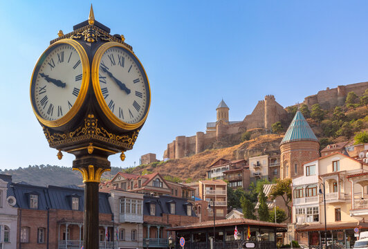 Street clock with Narikala Fortress, St. Nicholas Church and traditional architecture overlooking the Old Town in Tbilisi, Georgia.