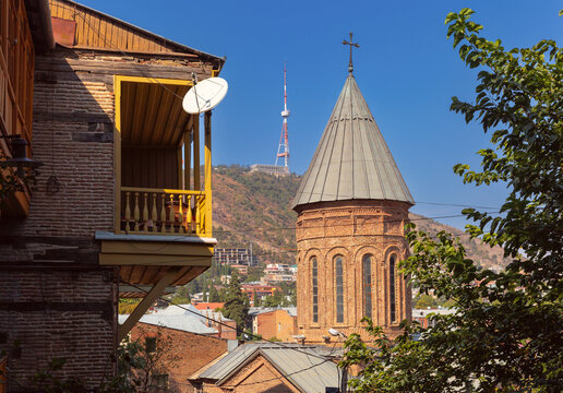 View of a medieval brick church with traditional balconies and the Tbilisi TV Tower rising above the historic district in Tbilisi, Georgia.