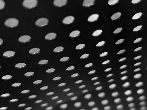 Perforated surface with repeating circular openings creates a pattern of light and shadow.