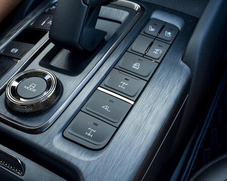 Close up of off-road drive mode control buttons, 4WD selector dial and seat heating controls on brushed metal car console panel