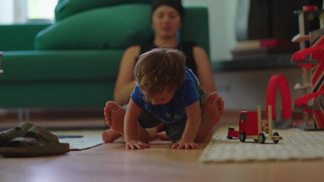 Toddler climbing off mother&rsquo;s legs at home, highlighting gross motor development, active play and childhood independence