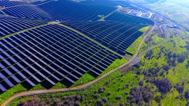 Aerial view of solar farm and substation. Overhead shot of electrical equipment beside panel rows amid green hilly countryside.