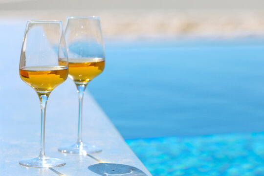 Two glasses of orange wine overlooking a pool and sea view in Santorini, Greece, capturing luxury travel, fine dining, and Mediterranean hospitality.