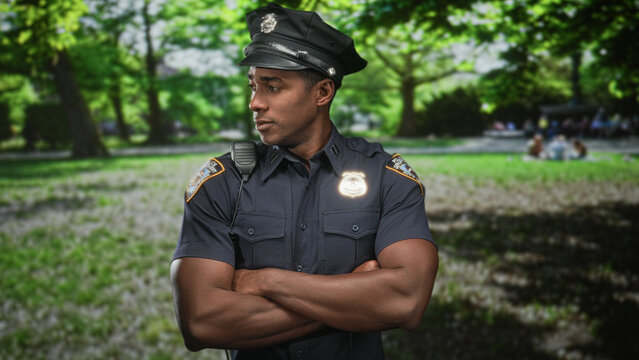 Police officer wearing cap and badge with radio, arms crossed and looking sideways in forest; confidence duty.