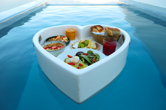 Floating breakfast tray in a luxury infinity pool in Santorini, Greece, featuring fresh fruit, pastries, juice, and gourmet breakfast items.
