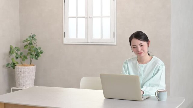 観葉植物のあるリビングでノートパソコンを使いながら笑顔を見せる日本人女性