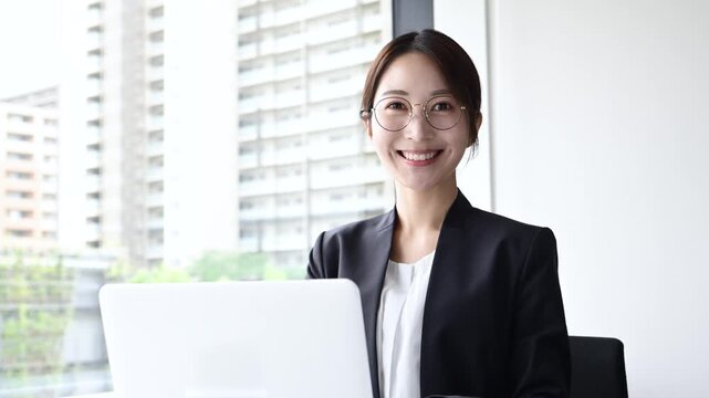 眼鏡をかけて笑顔でノートパソコンを使う20代日本人女性