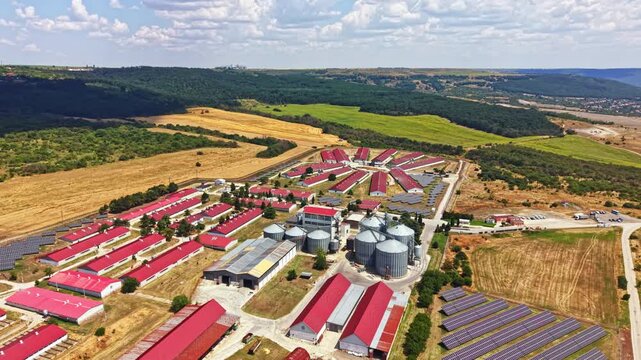 A large pig farm features several buildings with red roofs, silos, and fields. The scene shows the layout of the farm and surrounding landscape with green hills and open fields.
