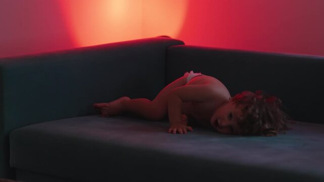 Toddler playfully falling into couch from armrest, highlighting fearless exploration, gross motor development and joyful childhood play at home