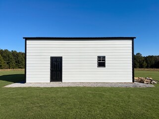 Obraz premium White Metal Garage with Double Doors and Black Accents in Open Green Field