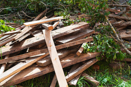 Wooden planks and branches are piled together in a grassy outdoor space, indicating recent yard work or landscaping.