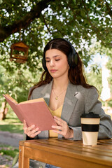 Fototapeta premium Charming young woman enjoying a sunny day reading while sipping coffee in a lovely park