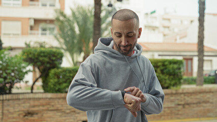 Fototapeta premium Man wearing hoodie and smartwatch making fists in a playful boxing gesture on a street with buildings and hedges; playful.