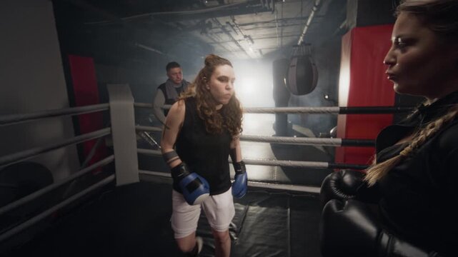 Caucasian young female boxers preparing to spar in ring while middle aged male coach watches. Footage suitable for fitness apps, sports marketing, and female empowerment campaigns