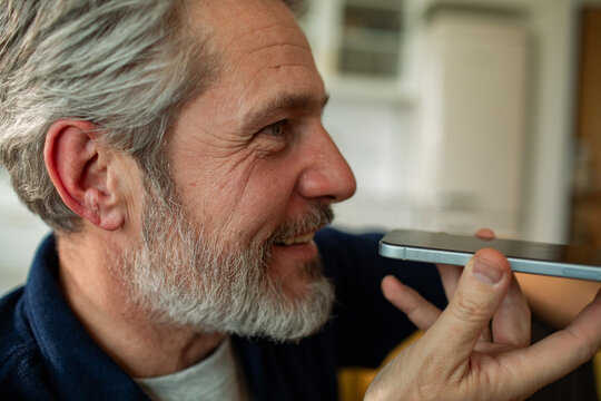 Smiling middle-aged man using smartphone voice assistant at home