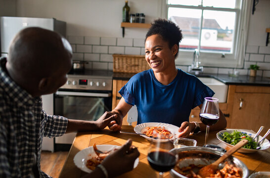 Smiling couple holding hands at pasta dinner in home kitchen