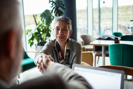 Smiling senior businesswoman shaking hands during meeting in modern cafe