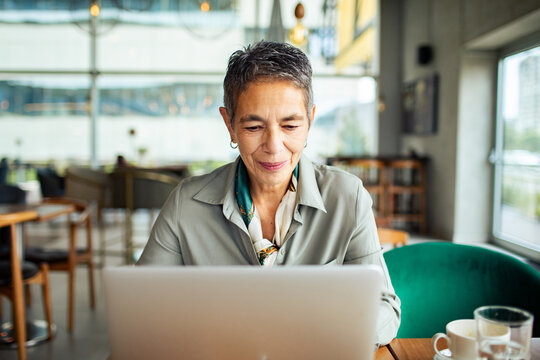Smiling senior woman working on laptop in cafe
