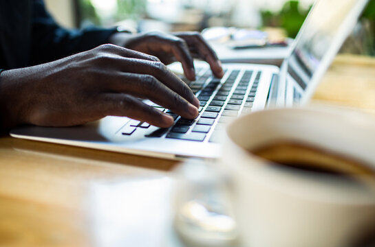 Close-up of hands typing on laptop at a cafe
