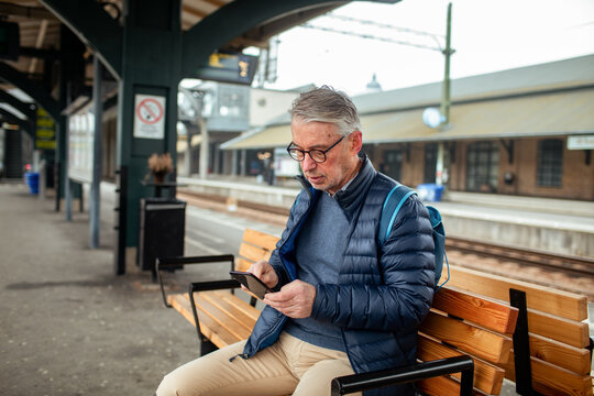Senior man using smartphone at train station platform