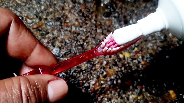 Close up of squeezing white toothpaste onto a red toothbrush bristles