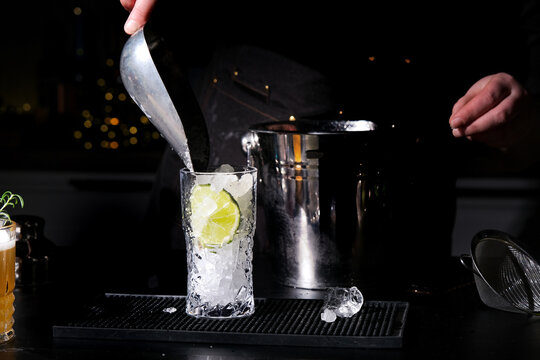 Ice scooping into highball glass with lime on bar counter. Caipirinha or mojito drink preparation with cachaca or rum.