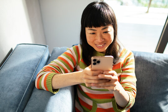 Smiling woman using smartphone on sofa at home