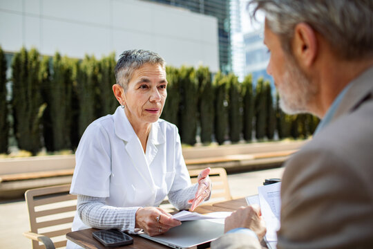 Senior healthcare professional advising patient outdoors at city hospital