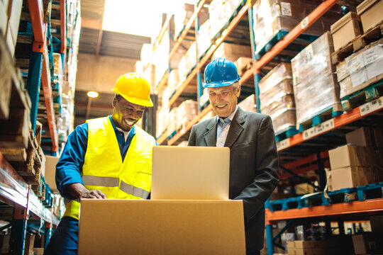 Warehouse manager and worker using laptop in distribution center