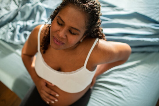Pregnant woman with back pain sitting on bed at home