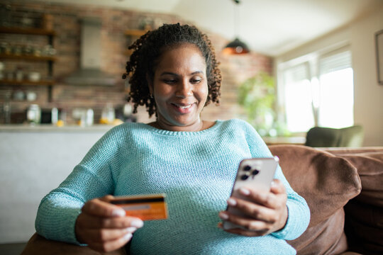 Smiling woman paying with credit card on smartphone at home