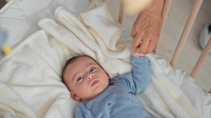 Newborn hispanic boy grasps an adult finger in a crib building, hand curled on a soft blanket, eyes focused upward  calm gentle bonding. © Krakenimages.com