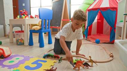 Boy kneeling and reaching with hand toward toy train on wooden floor in building playroom with tent, chair and foam puzzle mat  imaginative play joy. © Krakenimages.com