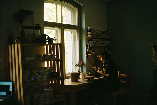 A ceramicist hand-paints pottery at a sunlit worktable