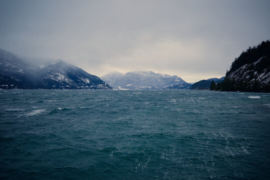 Large waves move in the water near rocky mountains on a winter day