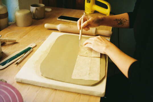Tattooed hands trace a pattern into fresh clay