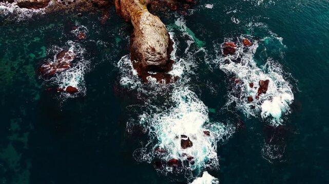 Aerial view of waves breaking on rocky outcrop. Overhead drone shot of turquoise sea, white foam and scattered boulder along Black Sea coast.