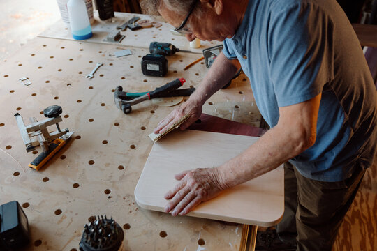 Elderly craftsman sanding a wooden board in a workshop
