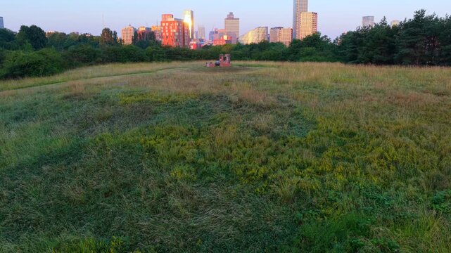 Aerial video overlooking lush green fields at Peachstone Henge towards Victoria Riverside, NOMA, and the glowing sunrise skyline of Manchester city centre.