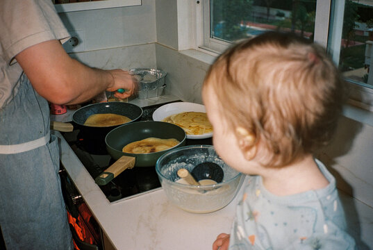 Anonymous baby looking at a father making pancakes