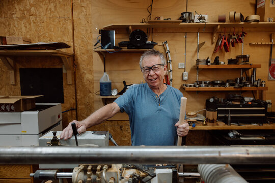 Smiling craftsman in woodshop holding dowel beside lathe