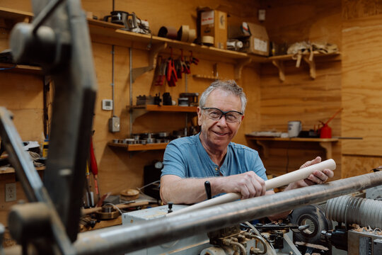 Candid senior woodworker smiling while turning a wooden dowel