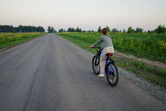 Woman riding bicycle on rural road at dusk