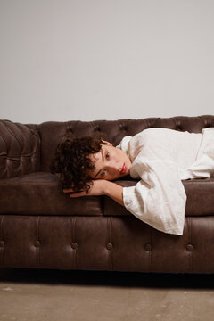 Woman Lying on Brown Couch in Simple Indoor Space 