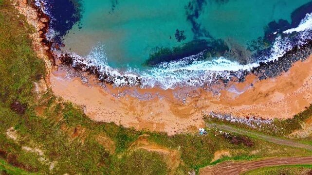 Aerial view of secluded cove with orange sand beach. Overhead drone shot of turquoise water, dark rock on shore.