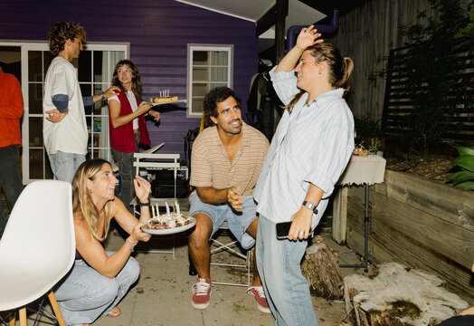 Friends bringing birthday cake to backyard night party